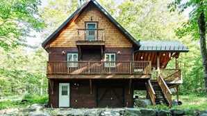 A two-story log cabin with a balcony, a covered porch, and a staircase leading to the upper level. - The Rustic - Nature retreat with Private SPA (Saint-Adolphe-d'Howard)