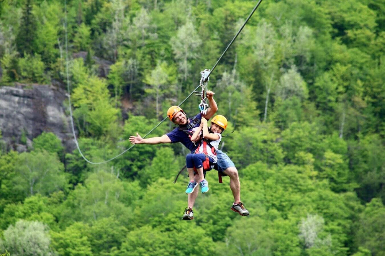Zwei Personen sausen mit einer Zipline durch einen bewaldeten Bereich.