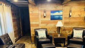 A cozy lounge area with leather sofas and ottomans, a wooden floor, and a view of the ocean through a large window. - Rustic Cozy cabin with water and dock access  (Florien)