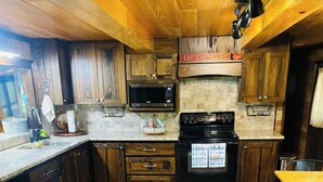 A kitchen with wooden cabinets, a microwave, a stove, and a dining area with a table and chairs. - Rustic Cozy cabin with water and dock access  (Florien)