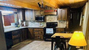 A cozy kitchen with wooden cabinets, a microwave, and a stove. There's a dining area with a table and chairs, and a sofa with a lamp. - Rustic Cozy cabin with water and dock access  (Florien)