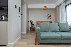 A modern living room with a sofa, a wooden headboard, a small side table, and a hanging light fixture.