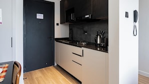 Una cucina compatta con una porta nera, una macchina da caffè e un telefono appeso al muro.