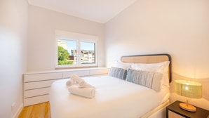 A bedroom with a large bed, a window with a city view, a bedside lamp, and a wooden floor. - GuestReady - A pinch of heaven in Lisbon (Lisbon)