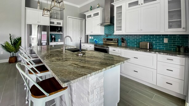 Una cucina moderna con mobili bianchi, un'isola in marmo e uno schienale color petrolio.