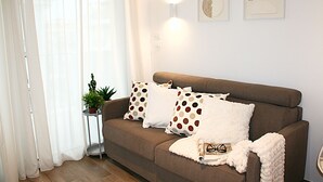Una sala de estar con un sofá marrón, almohadones blancos y marrones con lunares, una manta blanca y una mesita auxiliar con una planta.