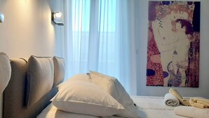 Un dormitorio con cama, almohadas, un adorno con forma de corazón, un cuadro y una ventana con cortinas.