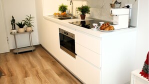 Una cocina moderna con armarios blancos, horno empotrado, cafetera y una planta pequeña en la encimera.