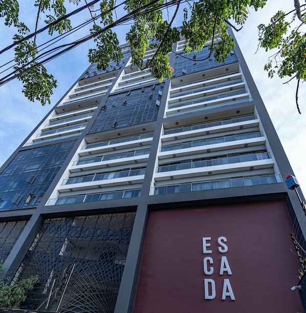 Un immeuble moderne de grande hauteur, doté de nombreux balcons et d’une enseigne rouge bien visible sur laquelle on peut lire « ES CADA ».
