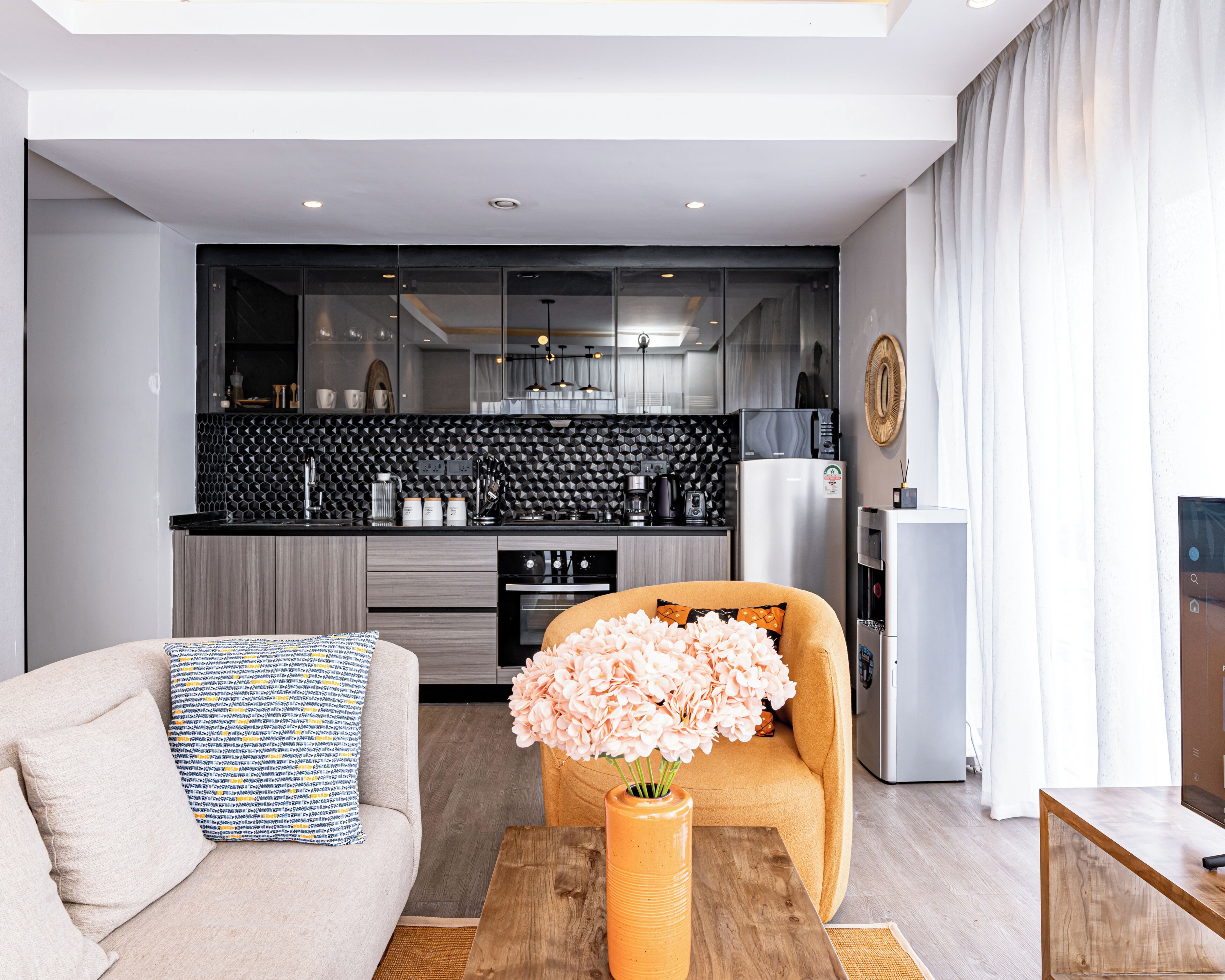 A modern living room with a sofa, a coffee table with a vase, and a kitchen in the background.