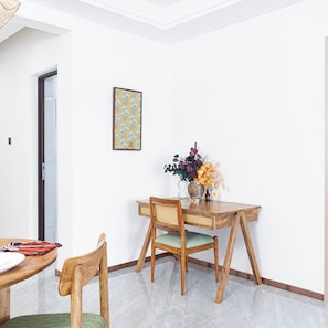 A dining area with a wooden table, two chairs, a vase with flowers, and a framed picture on the wall.
