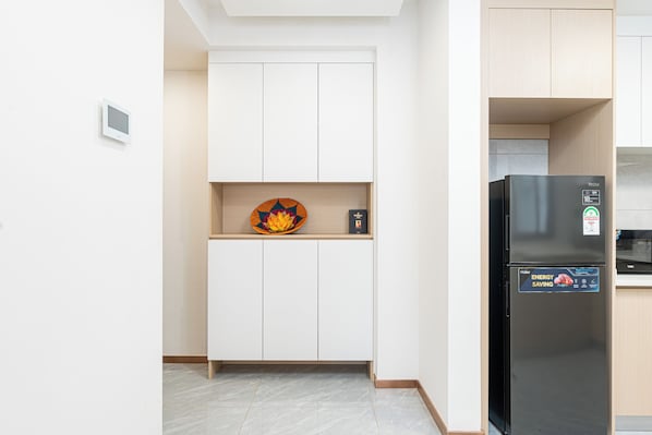 A compact kitchen with white cabinets, a black refrigerator, and a small shelf with decorative items.