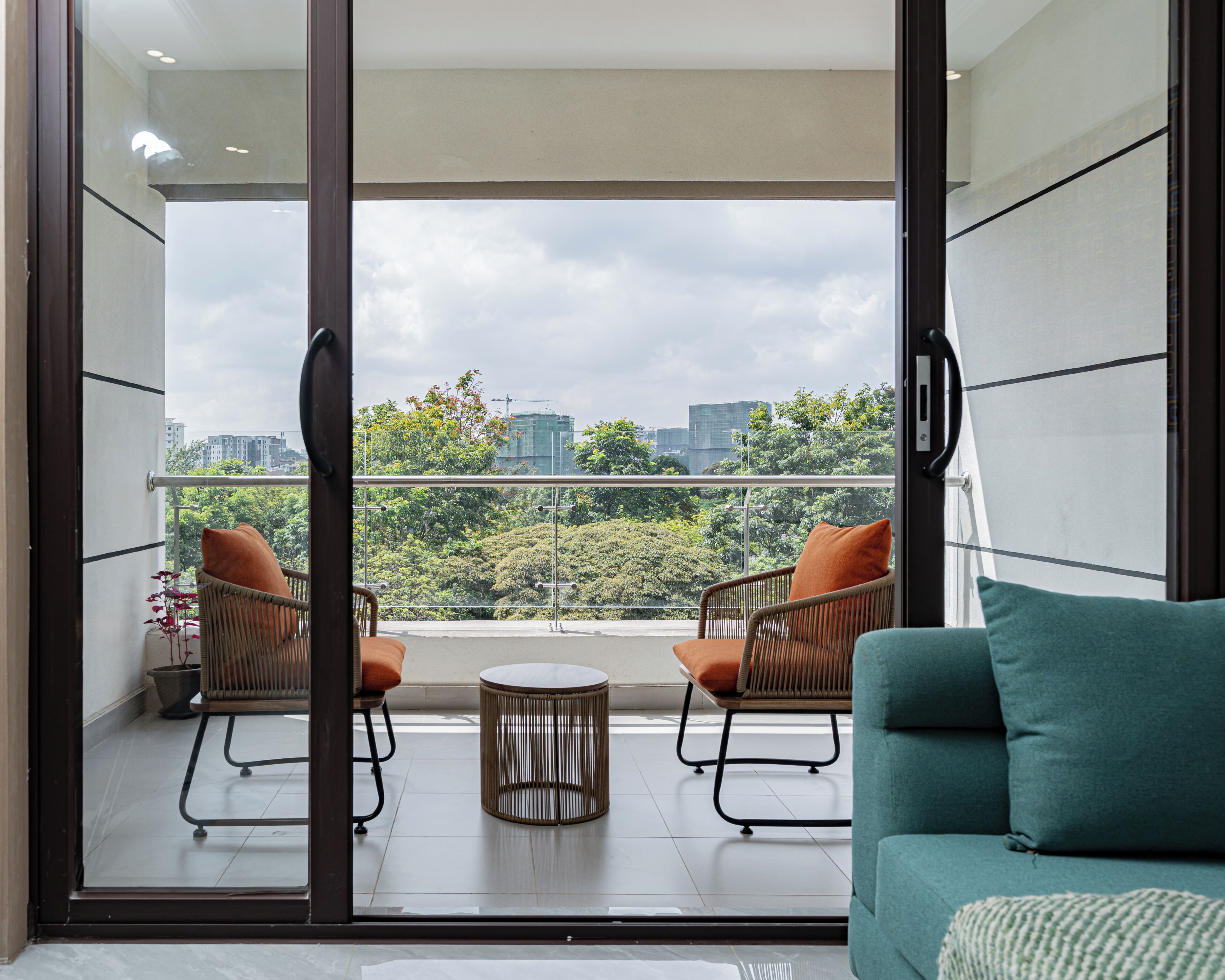 A balcony with two wicker chairs, a small round table, and a teal sofa.