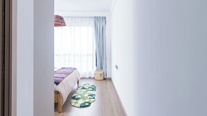 A room with a bed, a window with sheer curtains, a wooden floor, and a small woven basket. - 2 Bedroom - Spacious and Modern - Riverside One (Nairobi)
