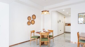 A dining area with a round table, four wooden chairs with green cushions, and a hanging light fixture. - 2 Bedroom - Spacious and Modern - Riverside One (Nairobi)