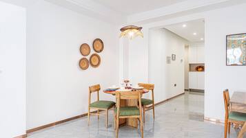 Un comedor con una mesa redonda, cuatro sillas de madera con cojines verdes y una lámpara colgante.