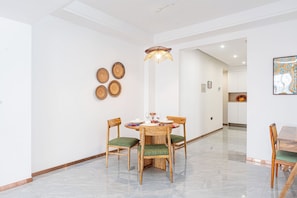A dining area with a round table, four wooden chairs with green cushions, and a hanging light fixture.