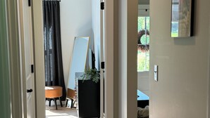 Een gang met een vloerkleed, houten vloer, een zwart kastje, een spiegel en een schilderij aan de muur.