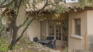 An outdoor patio with a table and chairs, a tree, and a building with a tiled roof and windows. - Air-conditioned Mazet Romarin - private terrace- shared swimming pool- Vallée des Baux (Paradou)