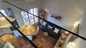 A spacious living area with a sofa, a dining table, and a large window providing a view of the outdoors. - Air-conditioned Mazet Romarin - private terrace- shared swimming pool- Vallée des Baux (Paradou)
