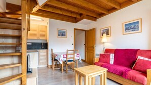 A cozy room with a wooden ceiling, a red sofa, a wooden table, and a dining area with chairs and a tablecloth.