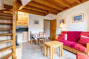 A cozy room with a wooden ceiling, a red sofa, a wooden table, and a dining area with chairs and a tablecloth.