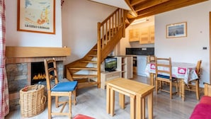 A cozy living room with a fireplace, wooden staircase, and a dining area with a table and chairs.