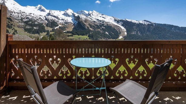 A balcony with a table and chairs, overlooking snow-capped mountains.