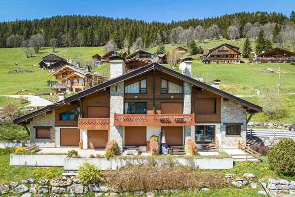 A large wooden chalet with a stone facade, multiple balconies, and a view of a green valley.