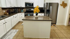 A kitchen with white cabinets, stainless steel appliances, a granite countertop, and a decorative Texas state map. - Sandy Retreat for family and groups Austin (Round Rock)
