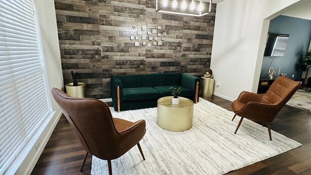 A modern living room with a green sofa, two brown armchairs, a white shag rug, and a wooden wall with a geometric pattern. - Sandy Retreat for family and groups Austin (Round Rock)