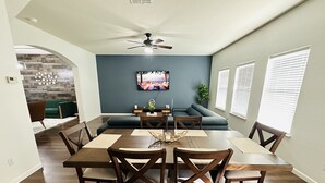 A dining area with a wooden table and chairs, a ceiling fan, and a blue accent wall. - Sandy Retreat for family and groups Austin (Round Rock)