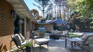 Un patio techado con mobiliario exterior, una parrilla y un gran paraguas que ofrece sombra.