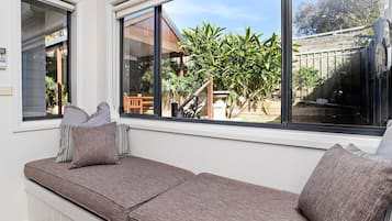 A window seat with cushions, a view of a garden, and a building in the background.