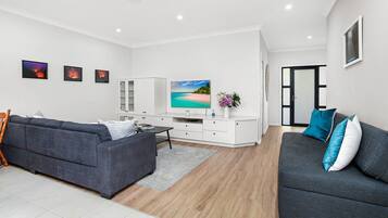 A modern living room with a grey sofa, a white cabinet, a flat-screen TV, and a wooden floor.