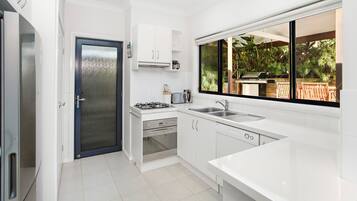 A modern kitchen with white cabinets, a gas stove, a built-in oven, and a large window overlooking a garden.
