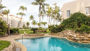 A resort pool area with a stone-lined pool, palm trees, and a view of the ocean.
