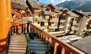 Een houten balkon met een tafel en stoelen, met uitzicht op een rij traditionele chalets met balkons, tegen een bergachtige achtergrond.