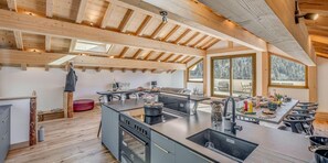 Moderni keittiö, jossa on keskeinen saareke, integroidut kodinkoneet ja suuret ikkunat, joista avautuu näkymä ulos.