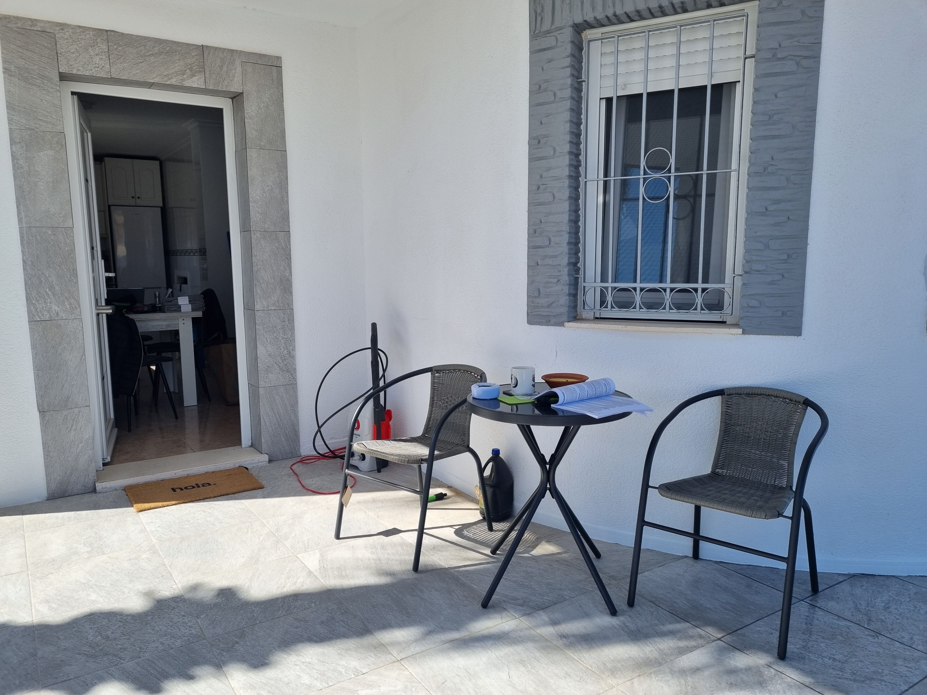 A room with a dining table, two chairs, a window with bars, and a door leading to another room.