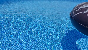 Piscina azzurra e trasparente con fondo piastrellato e un galleggiante gonfiabile scuro.