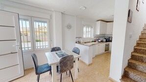 Una cucina compatta con mobili bianchi, un'isola centrale e un'area pranzo con due sedie e un tavolo.