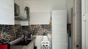 A compact kitchen with white cabinets, a patterned backsplash, a hanging light fixture, and a small stool. - Harmony in the green Veronese (Verona)