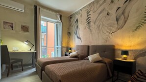 A hotel room with two beds, a desk, a chair, a lamp, and a mural on the wall. - Harmony in the green Veronese (Verona)