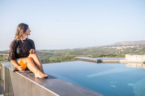 A person sitting by a clear pool with a view of a hilly landscape. - Villa Katrina – Villa with private pool (Kástellos)