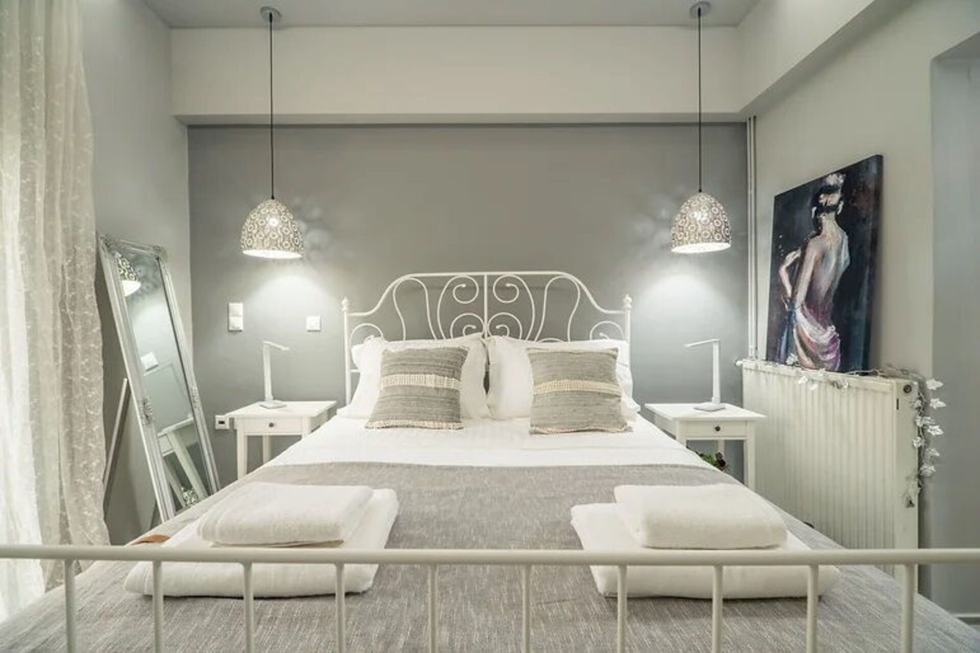 A modern bedroom with a large bed, two bedside tables, a radiator, and a painting on the wall.