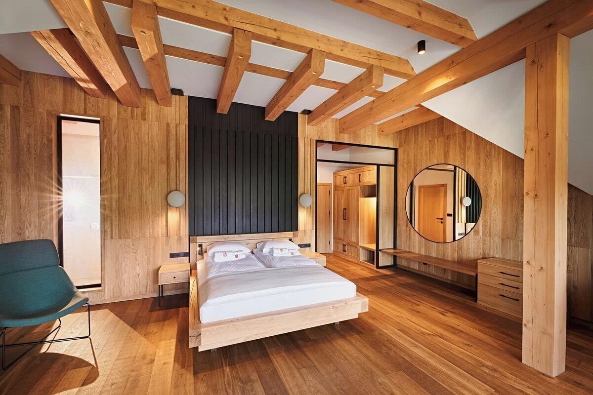 A modern bedroom with a wooden ceiling, a large bed, a bedside table, a chair, and a wardrobe.