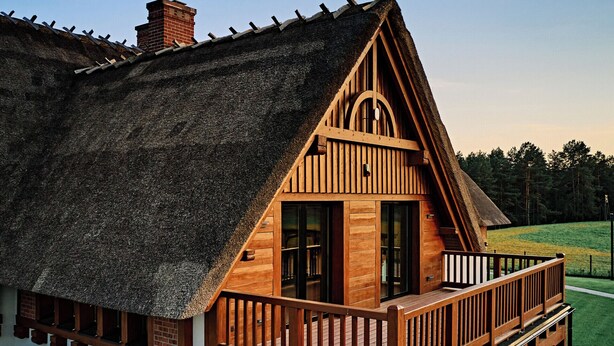 A wooden cabin with a thatched roof, a balcony, and a view of a green landscape. - Siedlisko Milachowo luxury wellness (Brusy)