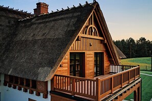 A wooden cabin with a thatched roof, a balcony, and a view of a green landscape. - Siedlisko Milachowo luxury wellness (Brusy)