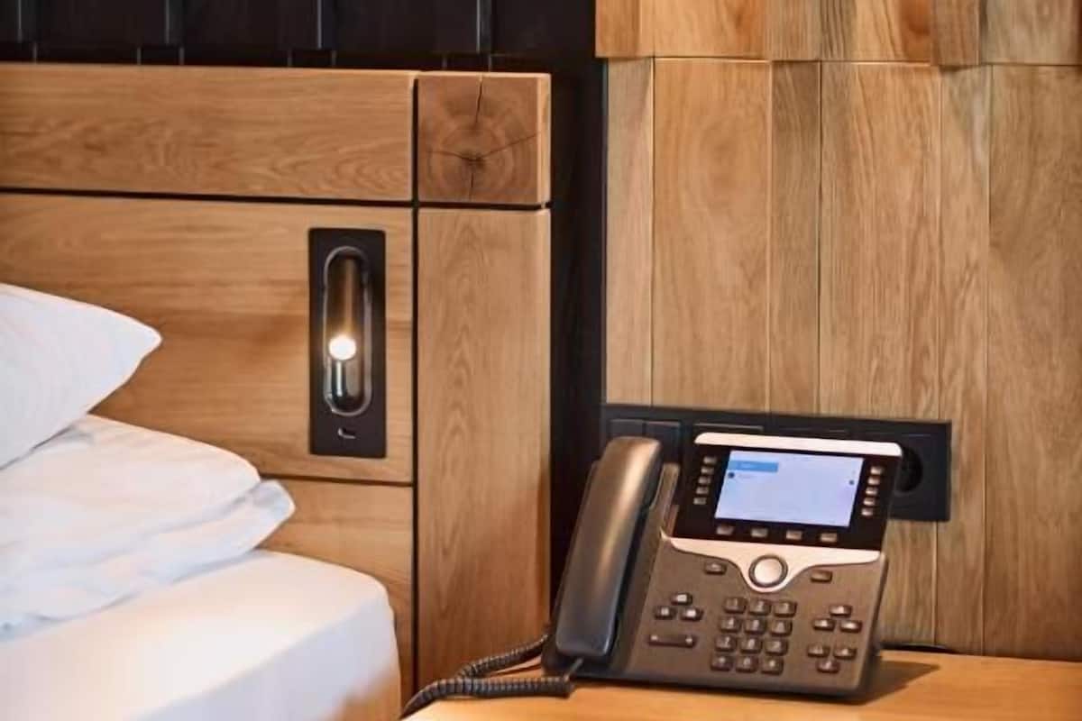 A hotel room with a wooden headboard, a bedside telephone, and a wall-mounted light fixture.